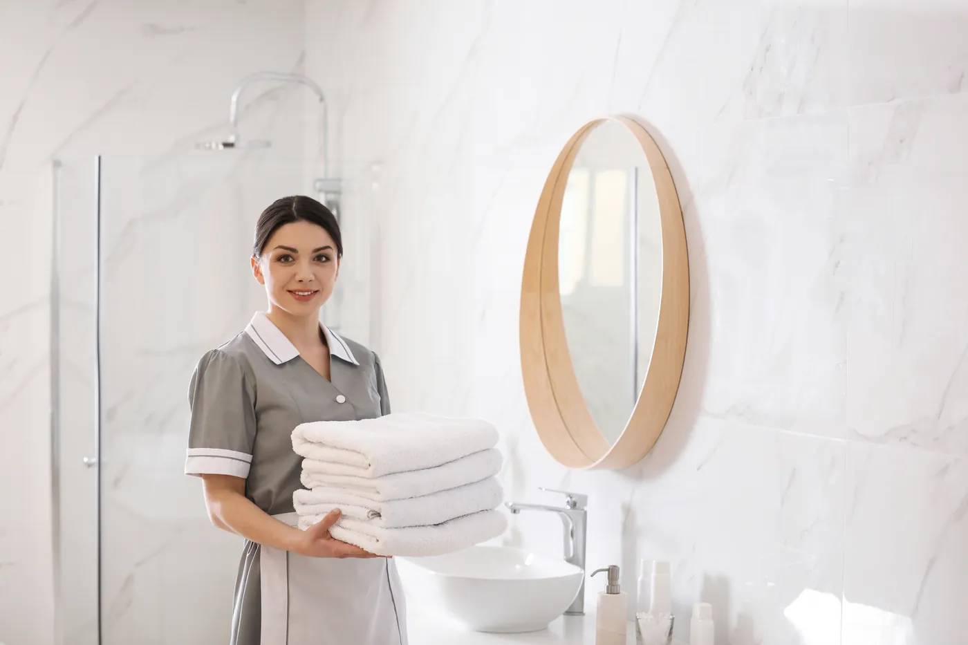 Une gouvernante NOBEL CLEAN tient une pile de linge plié dans une salle de bain d'hôtel